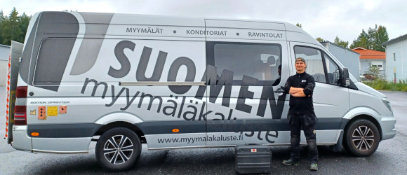 Huoltohenkilö seisoo Suomen myymäläkalusteen pakettiauton edessä.